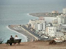 Rhodes, Greece 2019-Tourists sit on bench facing calm sea in Greece photo