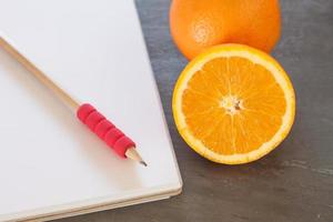 Pencil on a notebook next to oranges photo