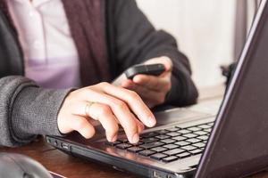 Person working on a laptop while looking at their phone photo