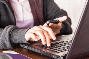 Close-up of a person holding a phone while typing on a laptop photo