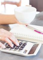 Person sipping coffee and using a calculator photo