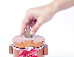 Primer plano de una mano colocando una moneda en una caja de dinero foto