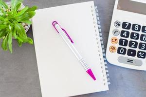 Calculator, notepad,  and pen with a green plant on a grey background photo