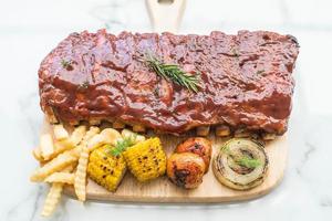 Grilled BBQ ribs with vegetables and french fries on wooden cutting board photo