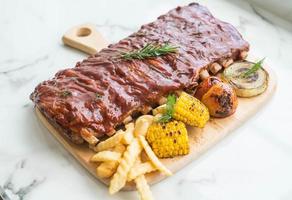 Grilled BBQ ribs with vegetables and french fries on wooden cutting board photo