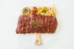 Grilled BBQ ribs with vegetables and french fries on wooden cutting board photo