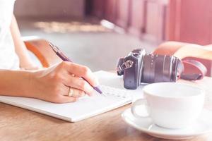 Woman writing in a notebook with a camera and coffee on a table photo