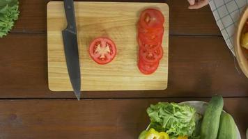 vista superior do chefe da mulher fazendo salada de alimentos saudáveis e picar tomate numa tábua na cozinha. video