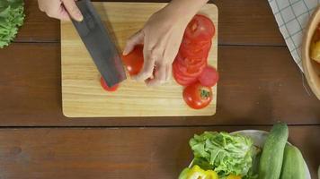 Top view of woman chief making salad healthy food and chopping tomato on cutting board in the kitchen. video
