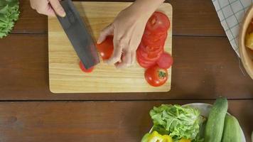 Draufsicht des Frauenchefs, der gesundes Essen des Salats macht und Tomate auf Schneidebrett in der Küche hackt. video