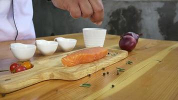 Nahaufnahme des Gourmetkochs oder des Kochs, der ein frisches Stück Lachsfisch mit Meersalz und gemahlenen würzigen Paprikaschoten würzt. video