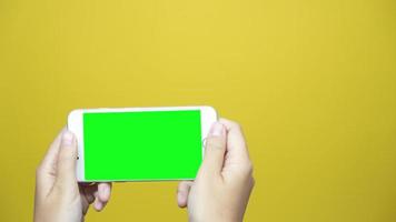 Woman using smart phone with green screen on yellow table background. Female hands scrolling pages, tapping on touch screen. video