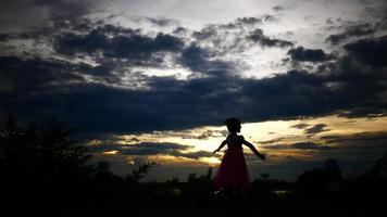 silhouet van een gelukkig klein meisje, wandelen met de ondergaande zon op de achtergrond