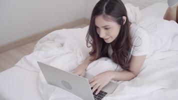 vacker asiatisk blandning ras kaukasisk kvinna med dator eller bärbar dator liggande på sängen i hennes sovrum. video