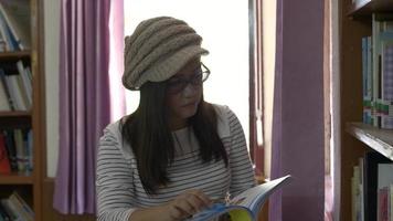 Woman standing at the behind of bookshelves and reading book in the university library. video