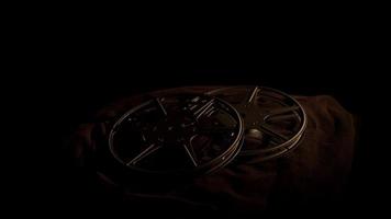 Film reels arrangement on black fabric and dark illumination spinning to the left in 4K video