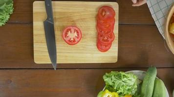 bovenaanzicht van chef-kok salade gezond voedsel maken en tomaten hakken op snijplank in de keuken. video