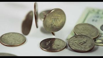  A lot of coins of quarter dollar falling over two coins and a $20 bill on white table, finally eight coins and the bill placed in the scene in 4K video