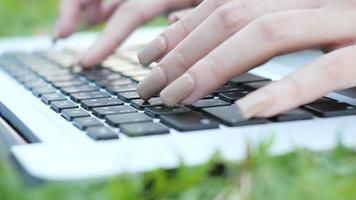 Young asian woman's legs on the green grass with open laptop. video