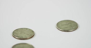 Four coins of quarter dollar falling over a lone coin on white table in 4K video