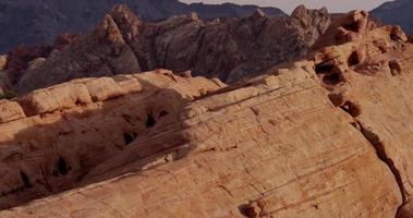 Vertical panning shot going up showing beautiful red rocks with different saturation in desert landscape with mountains in background in 4K ﻿ video