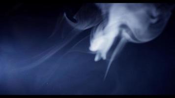 Soft white smoke defocused in foreground, focused in background and disappearing in darkness in 4K video