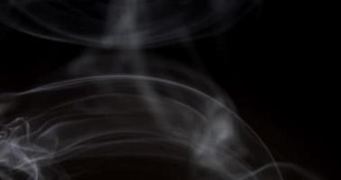 Soft thin lines of blurred white smoke dancing slowly on dark background in 4K video