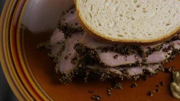 Foto giratoria de un delicioso sándwich de pastrami premium junto a una cucharada de mostaza de Dijon - comida 040