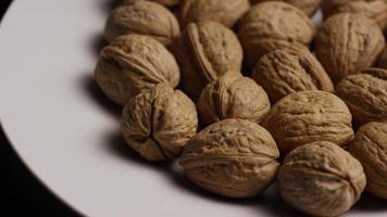 Cinematic, rotating shot of walnuts in their shells on a white surface - WALNUTS 013