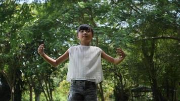 Petite fille asiatique jouant en plein air au ralenti, tournant et souriant et levant les mains en l'air video