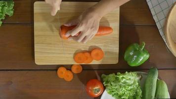 Draufsicht des Frauenchefs, der gesundes Essen des Salats macht und Karotte auf Schneidebrett in der Küche hackt. video