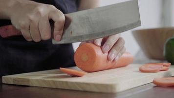 Close up of chief woman making salad healthy food and chopping carrot on cutting board in the kitchen. video