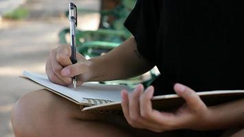 glad hipster ung asiatisk kvinna skriver i sin dagbok i park. video
