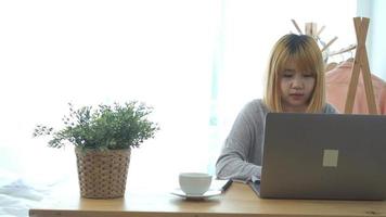 schöne junge lächelnde Frau, die auf Laptop kommt, während sie warmen Kaffee genießt, der in einem Wohnzimmer zu Hause sitzt. video