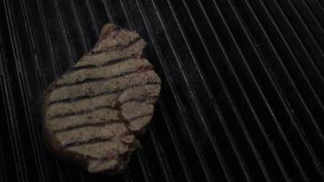 matlagning chef sätter okokt kött bit på het rökning grill med eld under med metallpincett, närbild slow motion. video