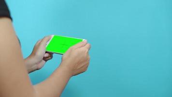 Woman using smart phone with green screen on blue table background. Female hands scrolling pages, tapping on touch screen.