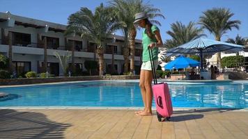 Young woman with pink case near swimming pool in hotel. Travel vacation concept video