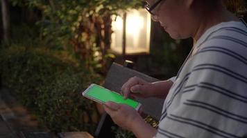 Woman hand with green screen in smart phone at garden in the evening.	 video