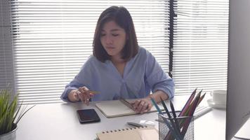 Asian woman in smart casual wear coming on computer while sitting on table in creative office. video