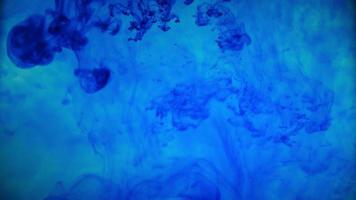 blaue Farbe Farbtinte strömt über das Glas mit fallenden Tintenbonbons und abstrakter Rauchexplosion.