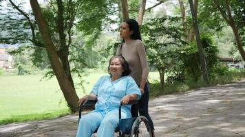 Older woman with her daughter pushing wheelchair around the park 