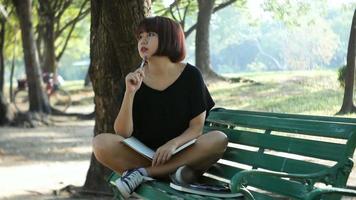 glad hipster ung asiatisk kvinna skriver i sin dagbok i park.
