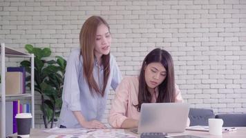 Two young Asian women coming together in an office at their small business sitting reading a report or papercom with pleased smiles. video