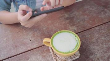 vrouwelijke blogger fotograferen van groene thee beker in café met haar telefoon. video