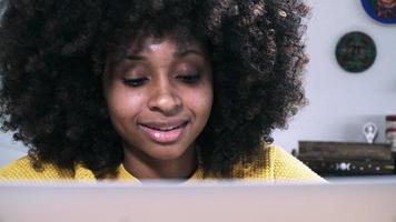 joven mujer negra sonriendo mientras escribe en una computadora portátil