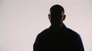 Silhouette of a young black man meditating and tilting his head up and then turning to the camera and finally turn to the left of the scene