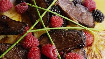 Rotating shot of a delicious smoked duck bacon dish with grilled pineapple, raspberries, blackberries, and honey - FOOD 108