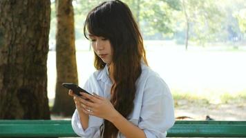 Jolie femme lit un message texte agréable sur téléphone mobile alors qu'il était assis dans le parc en chaude journée de printemps video