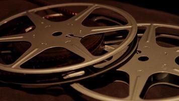 Close up to film reels arrangement on black surface and overhead illumination spinning to the left in 4K video