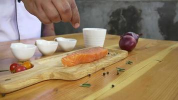 Close up di chef gourmet o cuocere condimento fresco pezzo di deli pezzo di salmone con sale marino e peperoni piccanti a terra. video